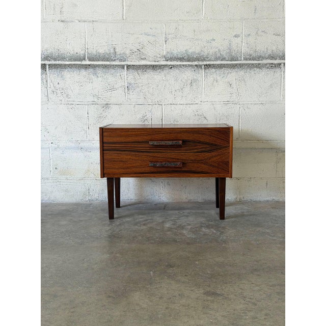 This minimalist lowboy features a compact rectangular silhouette elevated by four square tapered legs. The design...