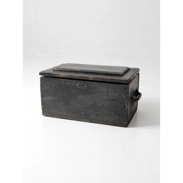 This is a vintage wooden tool box circa 1940s. The black wooden box features metal handles and a hinged closing lid. The...