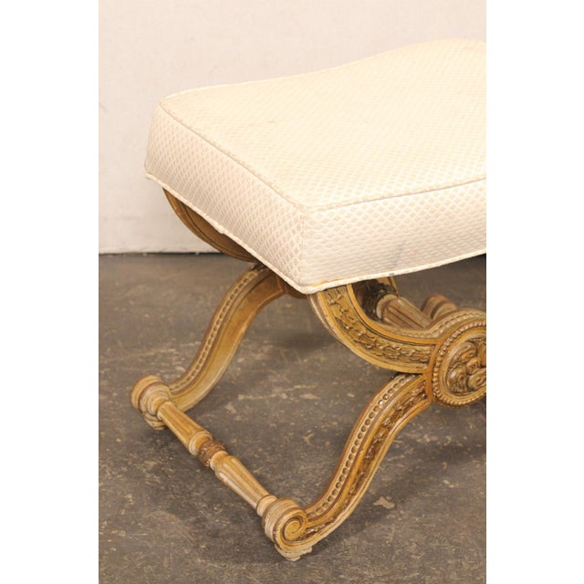 A French Louis XVI inspired carved wood curule stool, with upholstered seat, from the mid 20th century. This mid-century...
