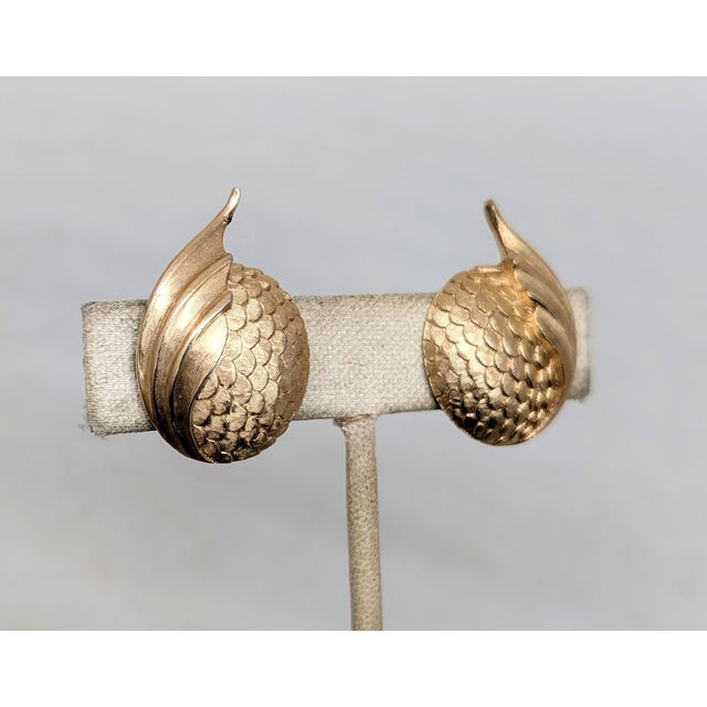 1960s goldtone round scaled texture with a leaf-like section sticking up on the side clip earrings. Marked "TRIFARI©" with...
