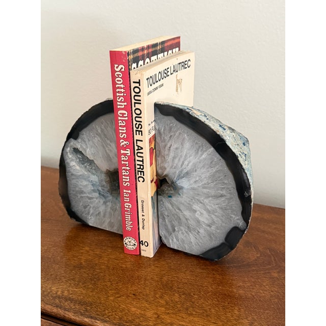 A pair of natural agate geode bookends with icy white crystal faces, gray green centers, and dark charcoal rims.