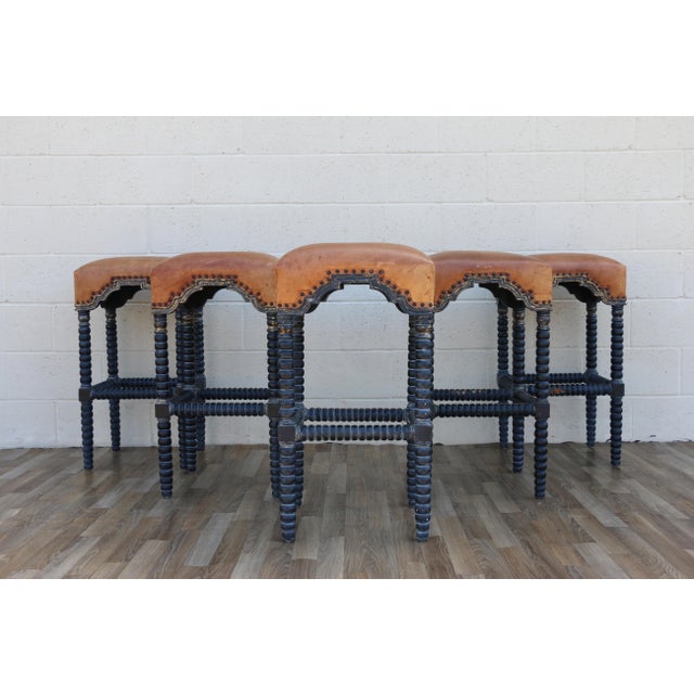 A striking set of five vintage bar stools featuring rich, distressed leather seats paired with beautifully turned solid...