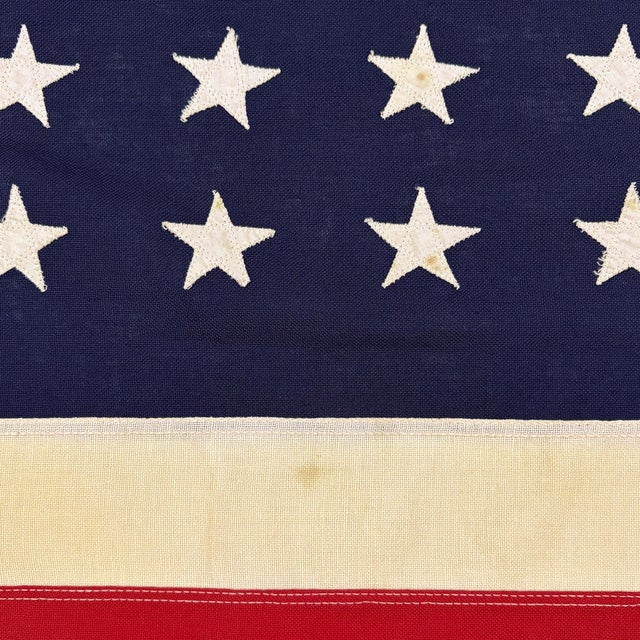 This vintage American flag is made from a cotton cloth with fully sewn stars and stripes. Please note staining, and other...
