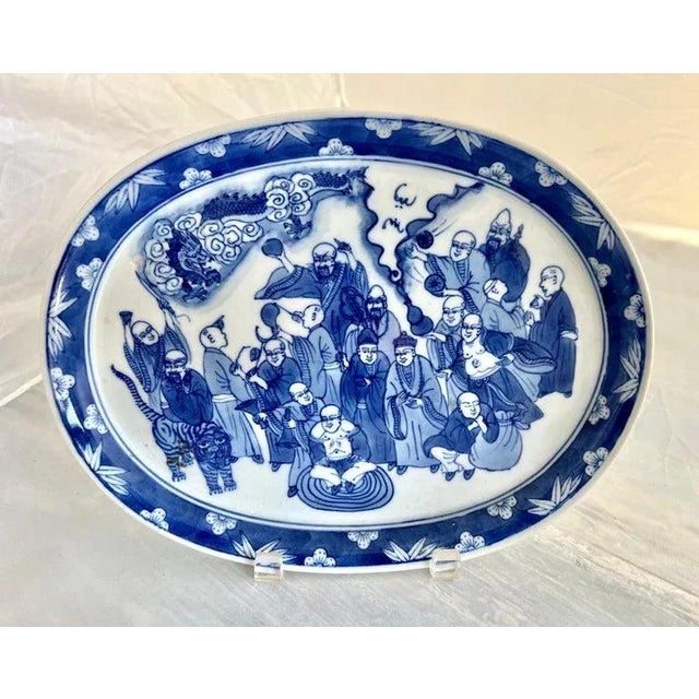 The Chinese export blue & white oval platter featuring depictions of wise men, a tiger, and a dragon likely reflects...