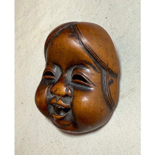 The Antique Japanese Hand Carved Boxwood Okame Noh Mask Mennetsuke is a beautifully crafted piece originating from Japan...