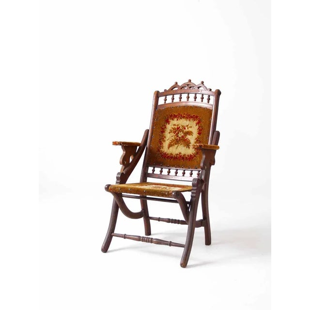 Late Victorian era folding lawn chair crafted from dark wood with an intricately carved top back slat. The seat is...