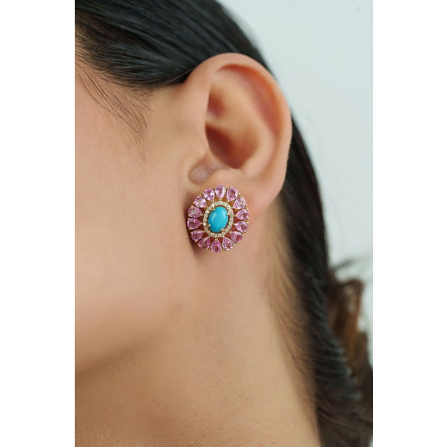 These floral halo stud earrings feature 6.32 carats of cabochon turquoise and pink sapphires set in 14K yellow gold and....