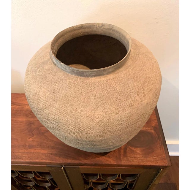 A pinkish stoneware jar with broad shoulder and slightly tapered body from Chinese East Zhou Dynasty (771-256BC). The...