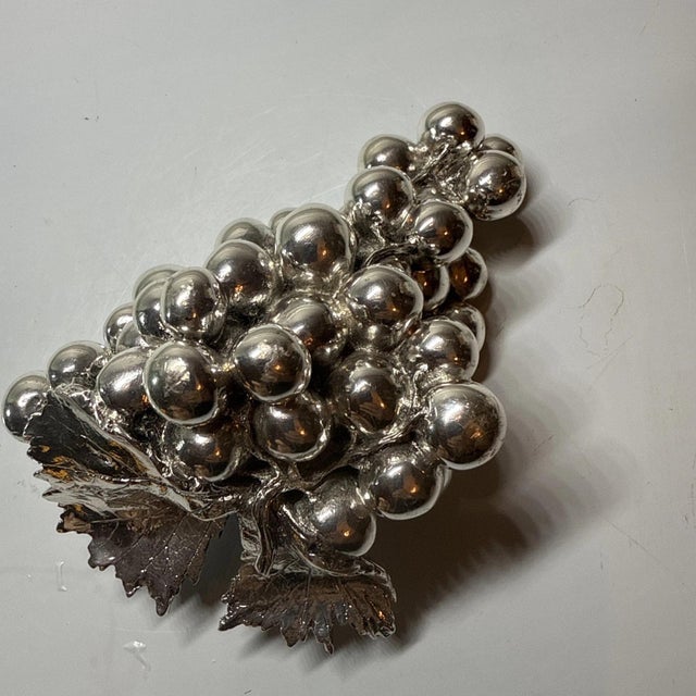 A Laminato AG grape cluster sculpture from Italy, in resin elegantly plated in 925 sterling silver, with green leaves. The...