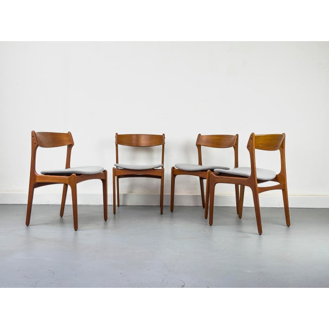 A set of four teak dining chairs with delicate, organic frames and upholstered seats, newly reupholstered in a light gray...
