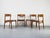 A set of four teak dining chairs with delicate, organic frames and upholstered seats, newly reupholstered in a light gray...