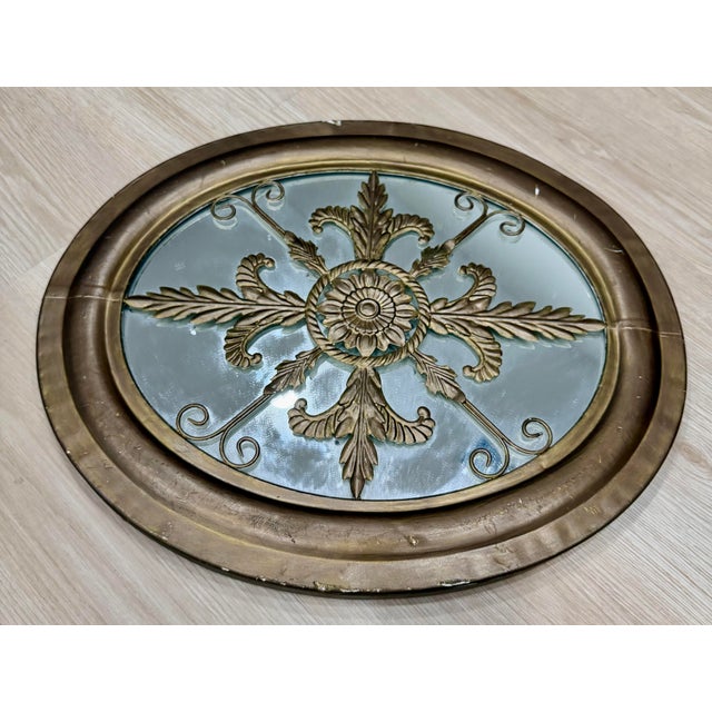 Elegant vintage oval mirror featuring an ornate giltwood frame with an intricate central floral medallion, scrolling...