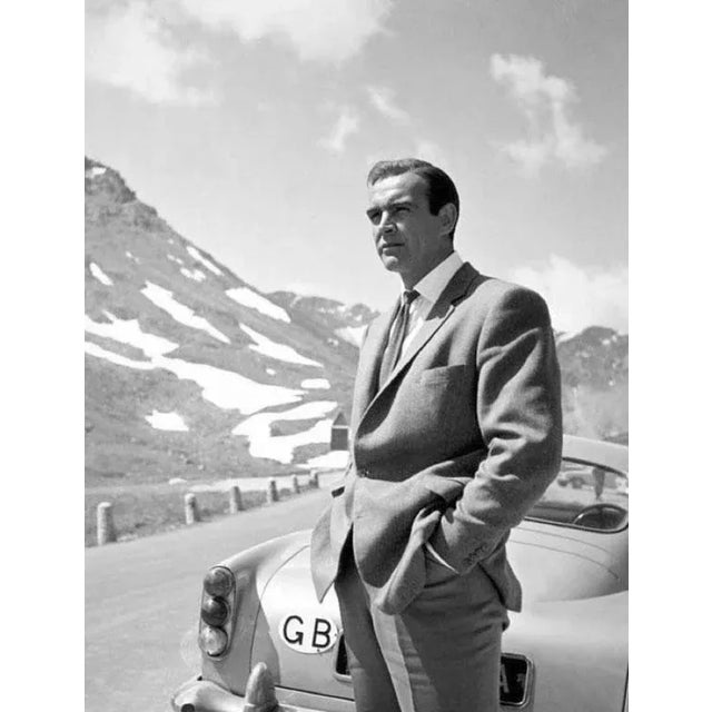 James Bond 007 Black Framed Sean Connery next to the infamous 007 silver Aston Martin DB5 car on a mountainous road in...