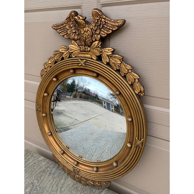 A gorgeous Federal or Regency style convex bullseye wall mirror featuring a carved eagle with open wings standing on olive...