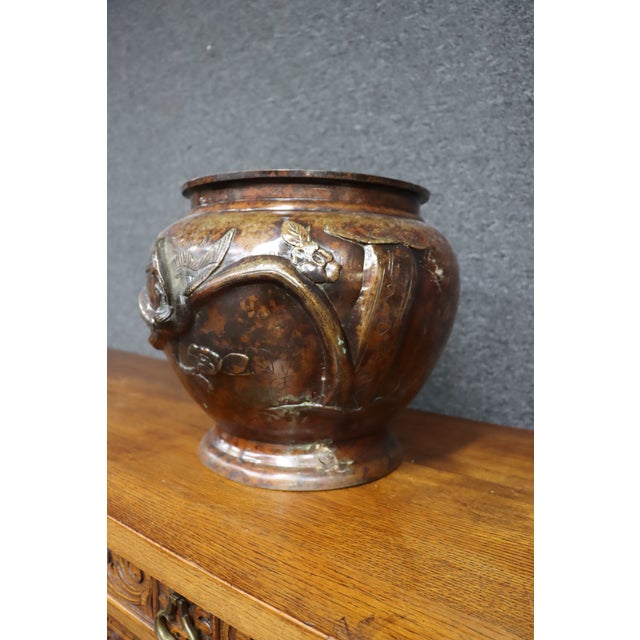 Japanese bronze jardinière featuring a rounded body, raised circular foot, and flared rim. The exterior is decorated with...