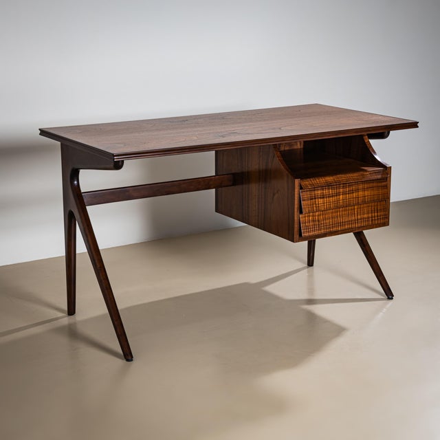 Mid-20th century desk featuring two drawers on the right side, flared legs, and a rectangular top with elegant profiling....