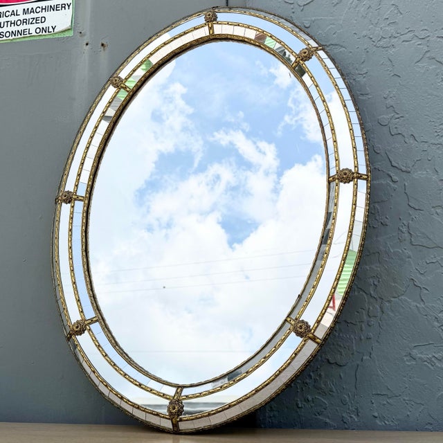 Elegant vintage Venetian-style oval wall mirror featuring a beautifully detailed gilt metal frame with mirrored border...