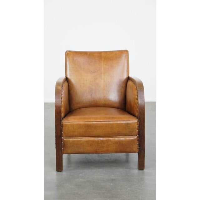 Offered is this unique and timeless cognac-colored sheep leather and wood Art Deco design armchair correctly finished with...
