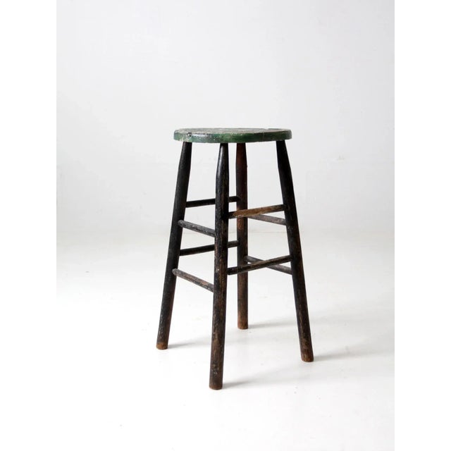 This is a rustic vintage wooden stool. The counter height stool features double stretchers and a round wooden seat. Black...