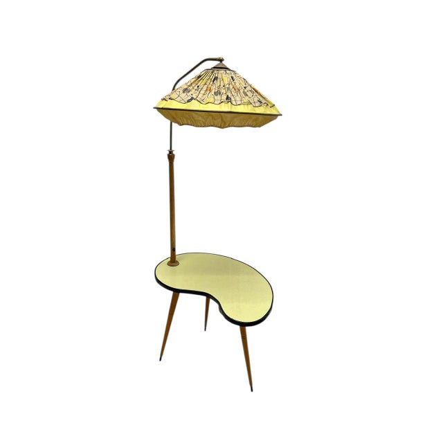 A typical 1950s side table with slender, tapered wooden legs and a kidney-shaped tabletop in yellow laminate with a black...