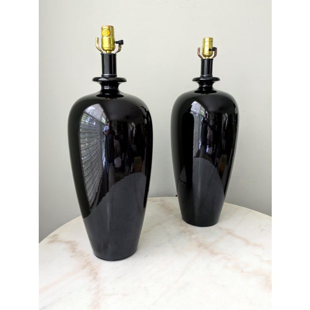 A pair of large vintage black ceramic lamps with a glossy finish. These classic urn-shaped lamps make a striking statement...
