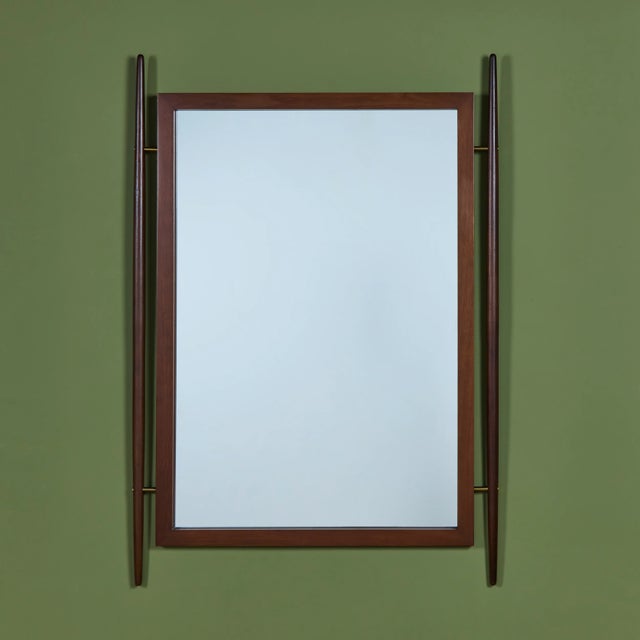 Rectangular walnut wall mirror, accented by walnut dowels along its vertical edges, all secured with brass hardware....