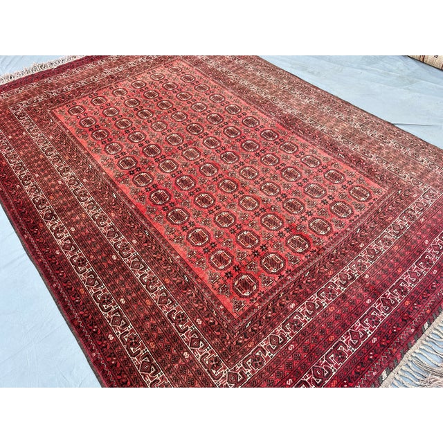 This refined Turkmen Bokhara rug presents a dense grid of small octagonal guls in deep burgundy and ivory, set against an...