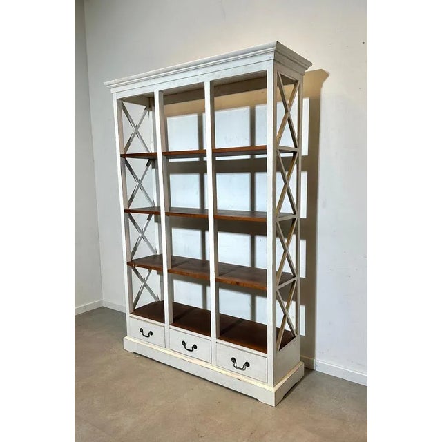 Elegant open bookshelf featuring a white painted frame with natural wood shelves and three lower drawers. The side cross...