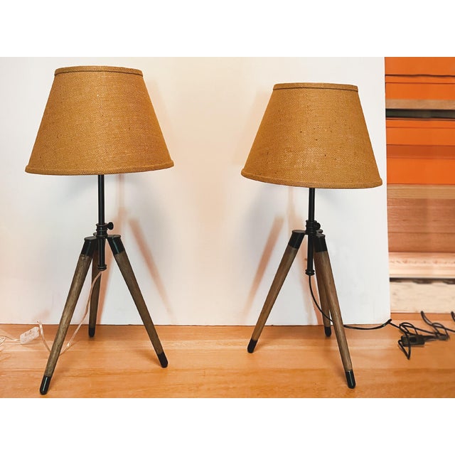 Pair of Irwin Surveyor tripod table lamps by Ralph Lauren, consisting of metal-trimmed wood legs and metal hardware. The...