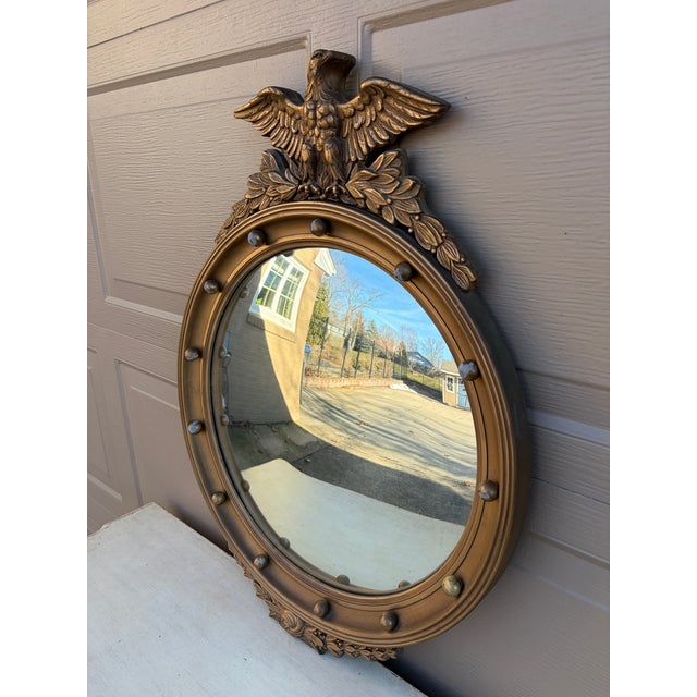A gorgeous Federal or Regency style convex bullseye wall mirror featuring a carved eagle with open wings standing on olive...