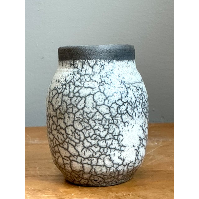 This vintage ceramic vase showcases the enduring beauty of traditional crackle glaze techniques, blending understated form...