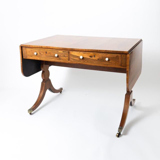 Late George III, English Adams' sofa table of faded Brazilian rosewood matched veneers. The rectangular table top is...