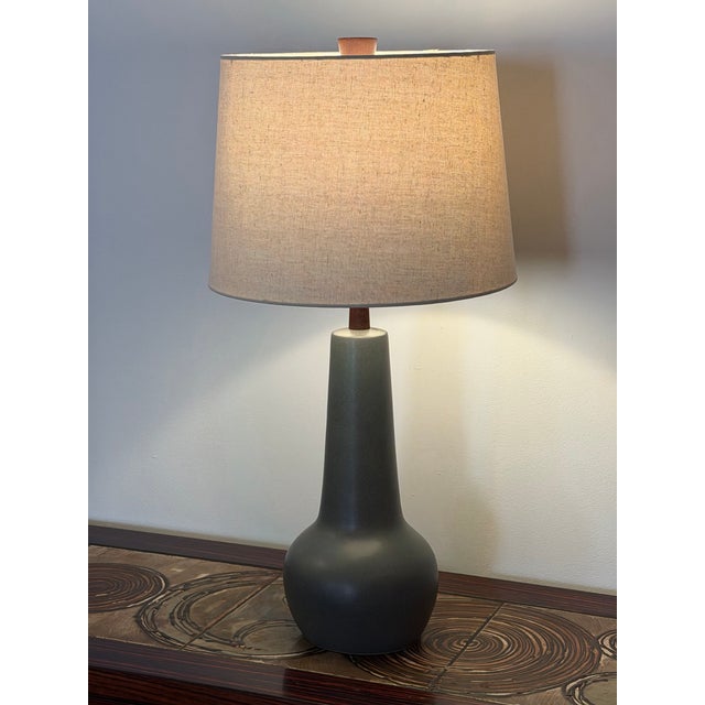 A ceramic table lamp by Gordon and Jane Martz with a rounded base, tall tapered neck, and matte gray-green glaze. The lamp...