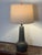 A ceramic table lamp by Gordon and Jane Martz with a rounded base, tall tapered neck, and matte gray-green glaze. The lamp...