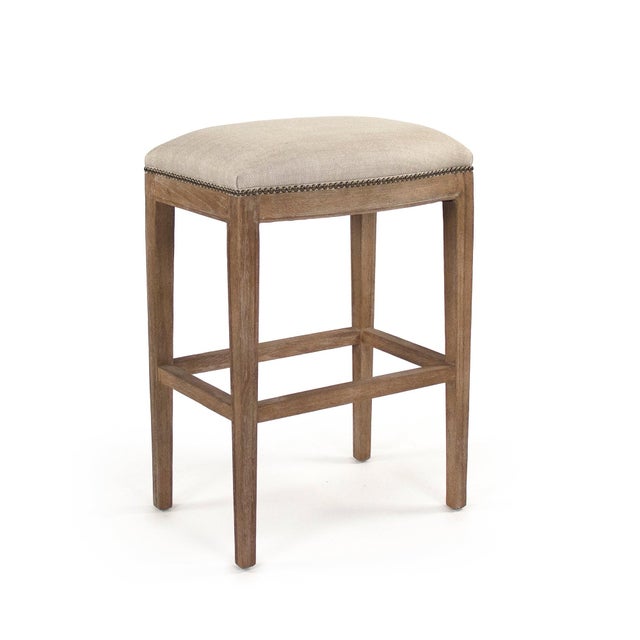 The Cora Bar Stool from Zentique is a clean-lined backless stool with a padded linen seat, brass nailhead trim, and...