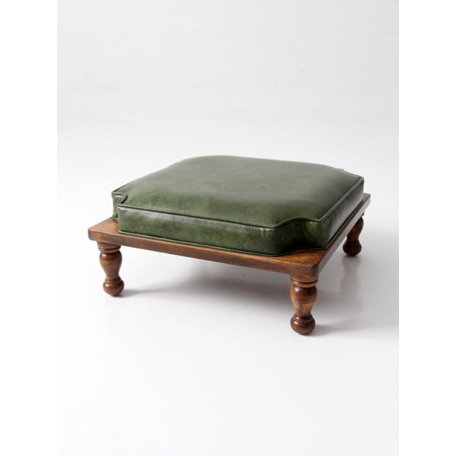 A mid-century Colonial Revival footstool with a square wood base and turned bun feet, topped with a tailored green faux...