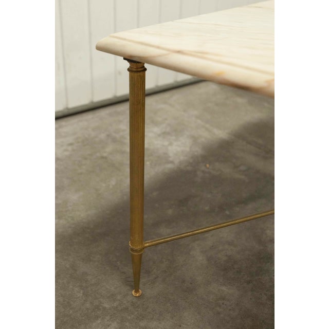 Marble and brass coffee table in the style of Maison Jansen. Metal base with screwed brass legs and a cross with a four-...