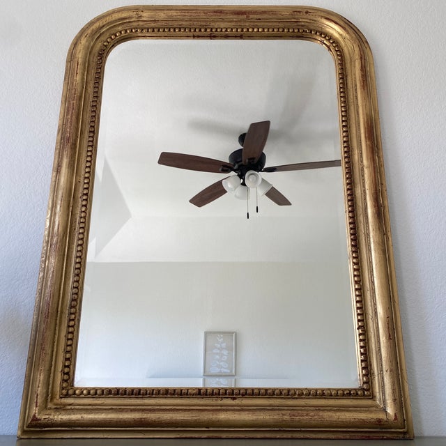 Louis Philippe French mirror with curved top edge. Framing finished in gold guilt with red undertones. Beveled edge glass.