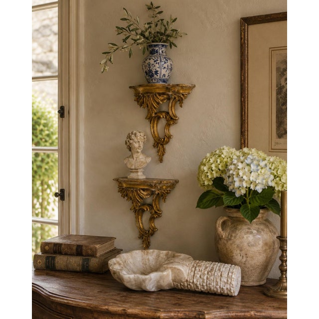 A decorative pair of mid-20th-century Italian wall shelves, hand carved in an open Rococo form with curling scrolls,...