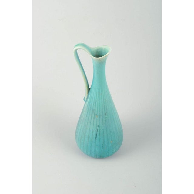 Pitcher in turquoise-blue glaze with ribbed body and elegantly curved handle. Designer: gunnar nylund manufacturer:...