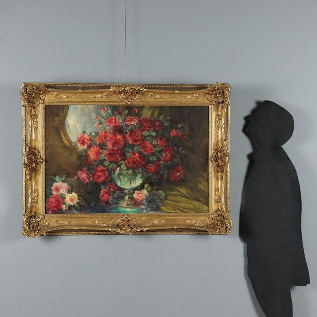 Oil on canvas. Signed lower right. A large bouquet of roses overflows from a crystal goblet vase, placed in front of a...