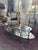 Striking vintage Hollywood Regency two-tier oval coffee table featuring sculptural glass supports, gilt metal accents, and...