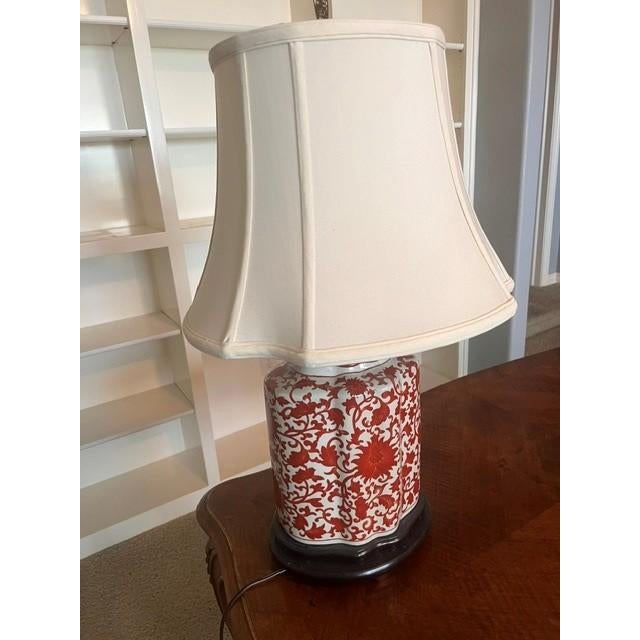 This elegant table lamp features a classic Chinoiserie-style porcelain base decorated with intricate red floral patterns...