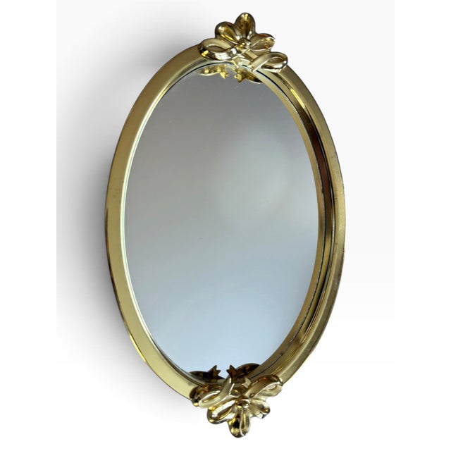 Elegant vintage mirrored vanity tray featuring a warm gold-tone metal frame with sculptural floral and bow-like...