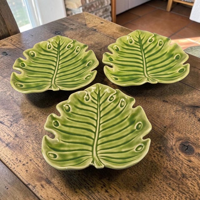 The product is a set of three ceramic serving plates in the shape of green Monstera leaves, designed by the brand...