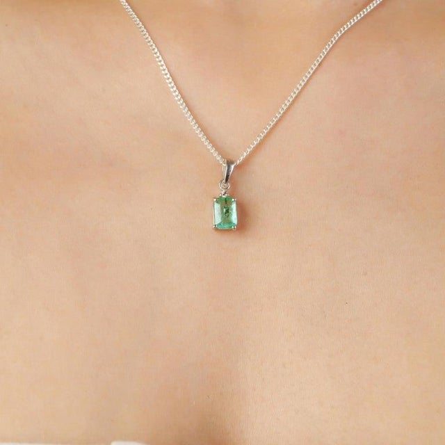 Crafted in 925 sterling silver, this emerald and diamond pendant features a beautifully cut emerald gemstone (4 x 6 mm,...