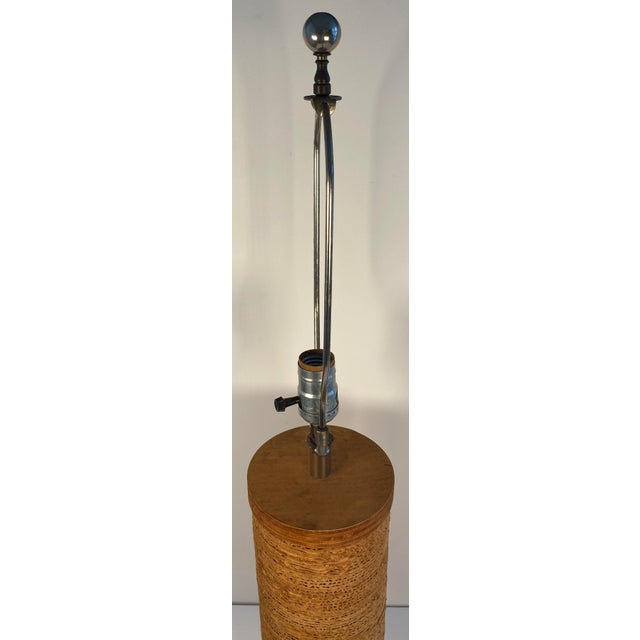 A handsome Mid-Century Modern table lamp featuring a tall cylindrical form wrapped in richly textured natural raffia or...