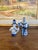A pair of vintage blue and white porcelain figurines depicting stylized folk figures in traditional dress. Each figure is...