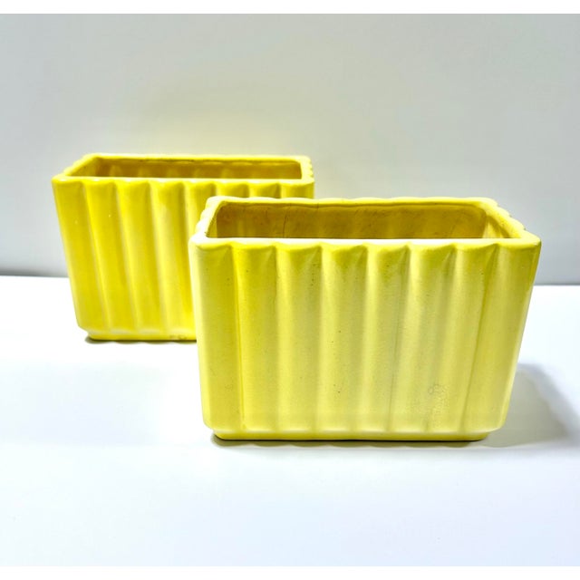 A vibrant pair of vintage ceramic planters featuring a bold sunny yellow glaze and sculptural fluted sides. Their clean...
