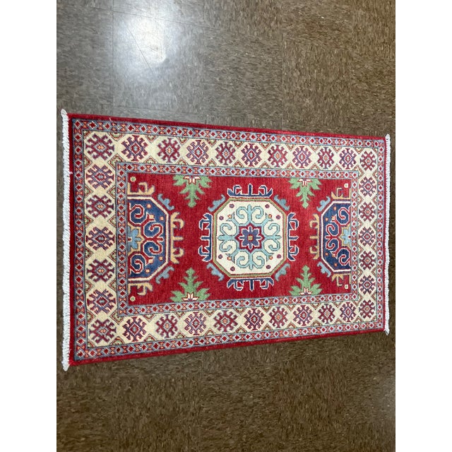 Hand-knotted Pakistani Kazak wool runner featuring a red field with a central geometric medallion and stylized tribal...